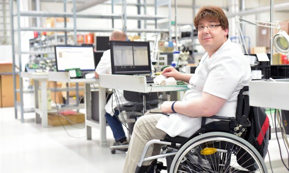 handicapped worker in a wheelchair assembling electronic components in a modern factory at the workplace 